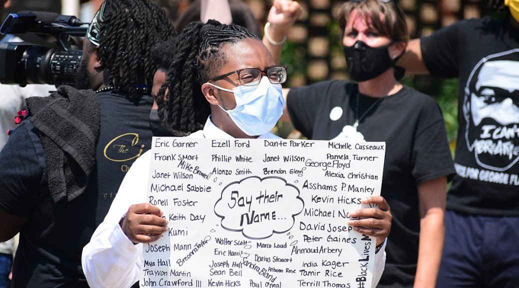 a man holding a sign with people of color killed by cops in the US at a BLM protest
