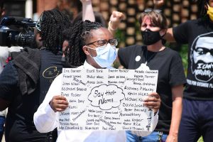 a man holding a sign with people of color killed by cops in the US at a BLM protest